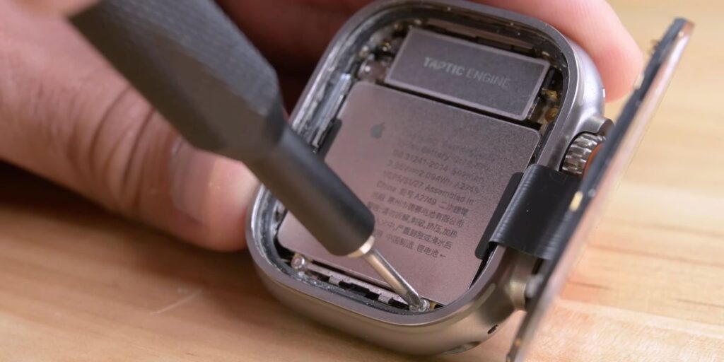A person using a screwdriver to disassemble a smartwatch, exposing the Taptic Engine and internal components