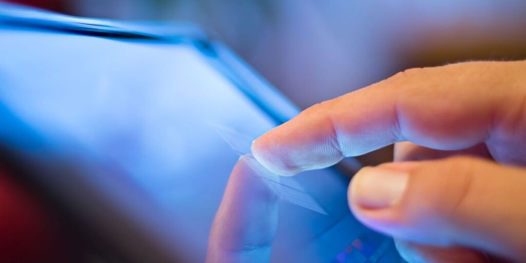 A close-up of a finger tapping on a touchscreen device, with the screen reflecting light in a soft, blurred focus
