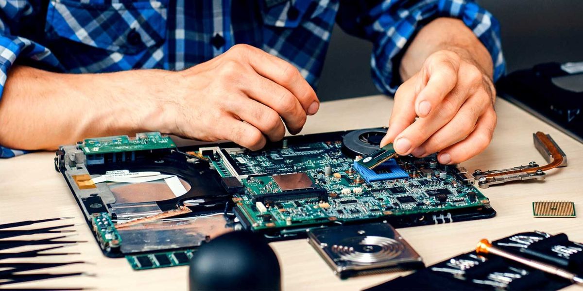 A technician's hands installing a component into a laptop motherboard during repair