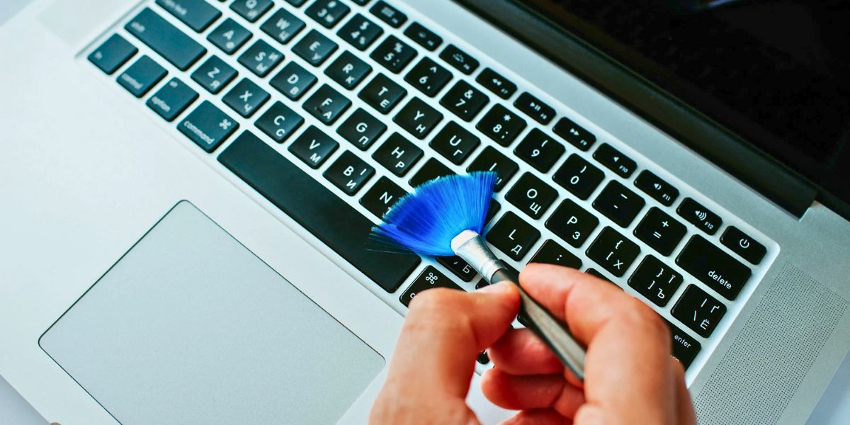 A hand holding a small blue brush cleaning the keys of a laptop keyboard.