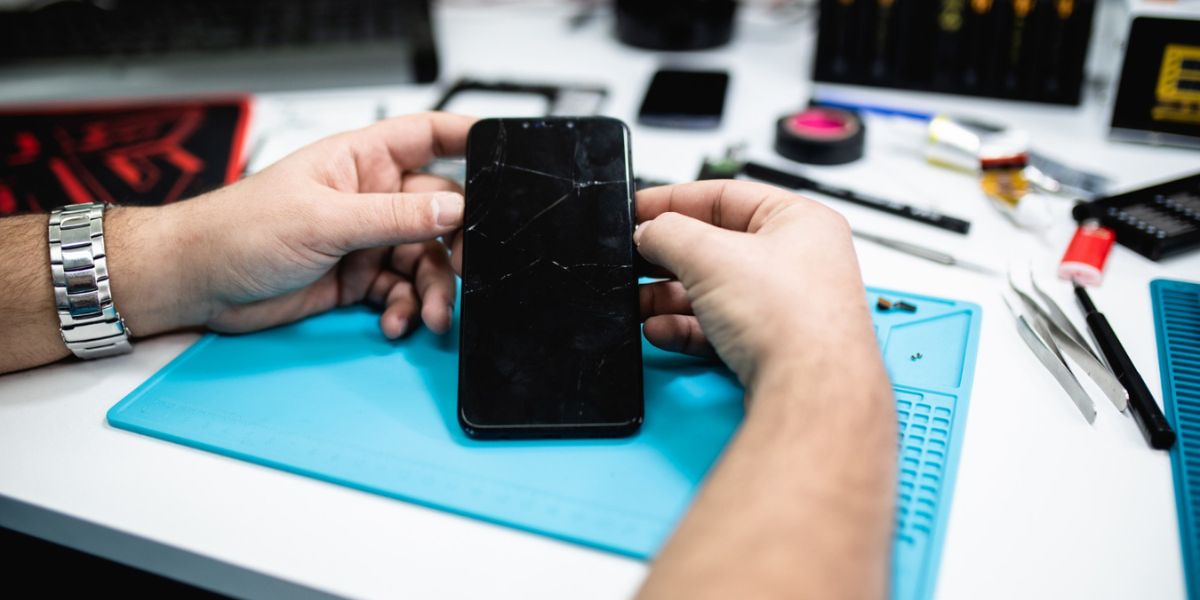 Close-up of a person's hands holding a smartphone being repaired over a blue workbench mat
