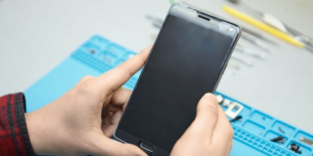 Technician in white gloves uses a magnifying glass and tweezers to repair a disassembled smartphone